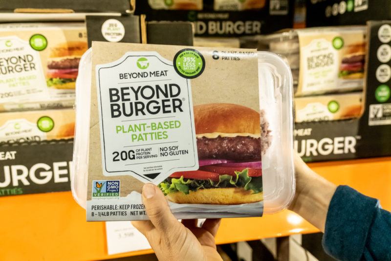 A person holding up a Beyond Burger container in the grocery store, with more behind them