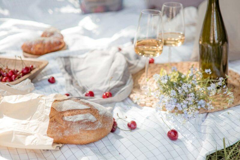 A picnic blanket with bread, glasses of wine, and cherries scattered across it