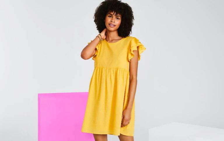 A young woman wearing a bright yellow dress from Haverdash in a mostly empty room