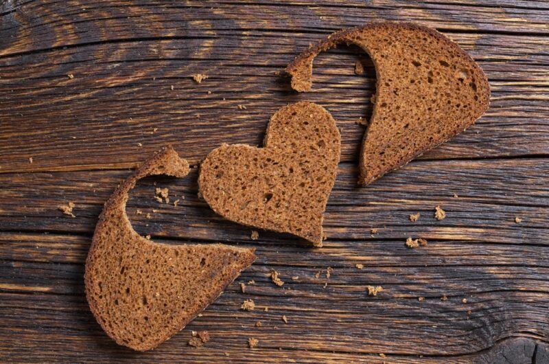 A wooden table with a slice of rye bread that has been cut to form a heart shape with two leftover pieces