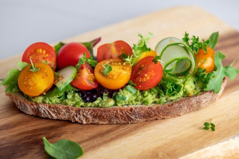 A slice of sourdough with mashed avocados, cucumber, and cherry tomatoes