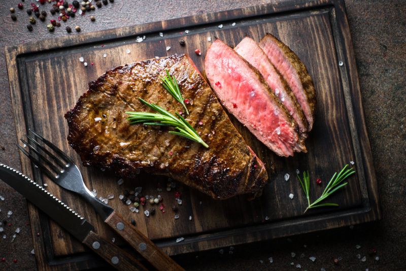 A large steak on a wooden board, where some pieces have been sliced off it