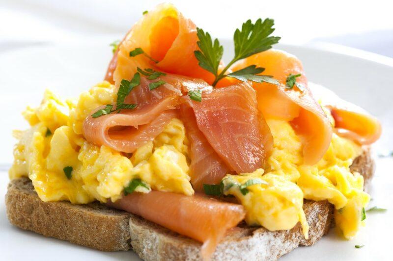 A piece of toast piled high with smoked salmon and eggs