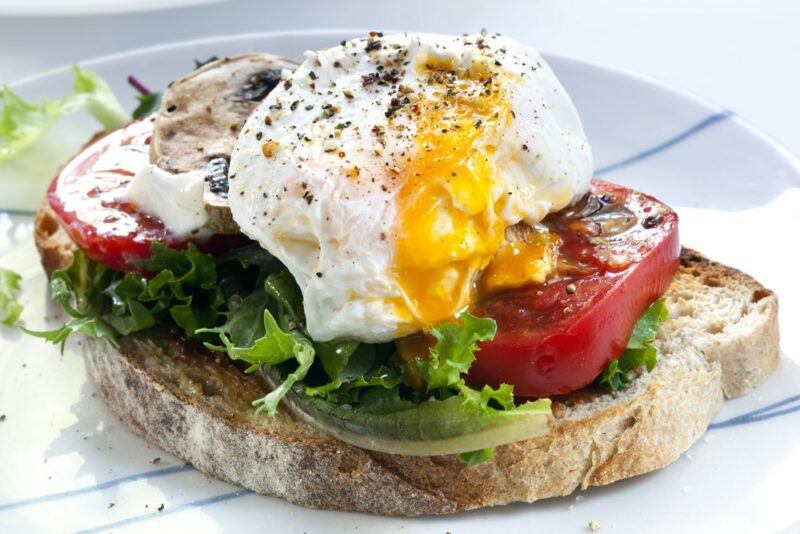 A white plate with a piece of sourdough, some greens, a tomato, and eggs