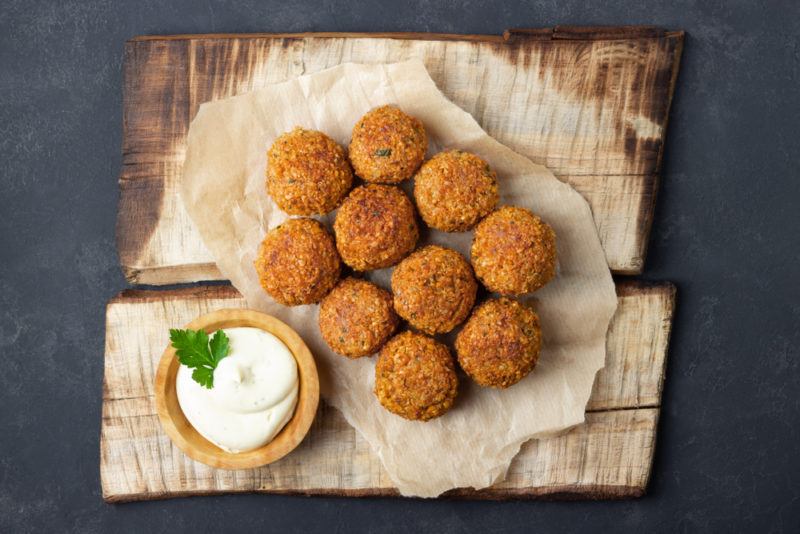 A pile of falafel on top of two wooden planks next to a small container of dip