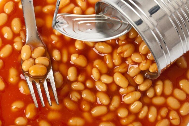 A pile of baked beans in tomato sauce, with a can and a fork