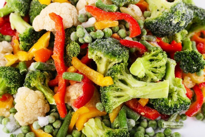 A pile of frozen vegetables, including bell peppers, peas, beans, and broccoli