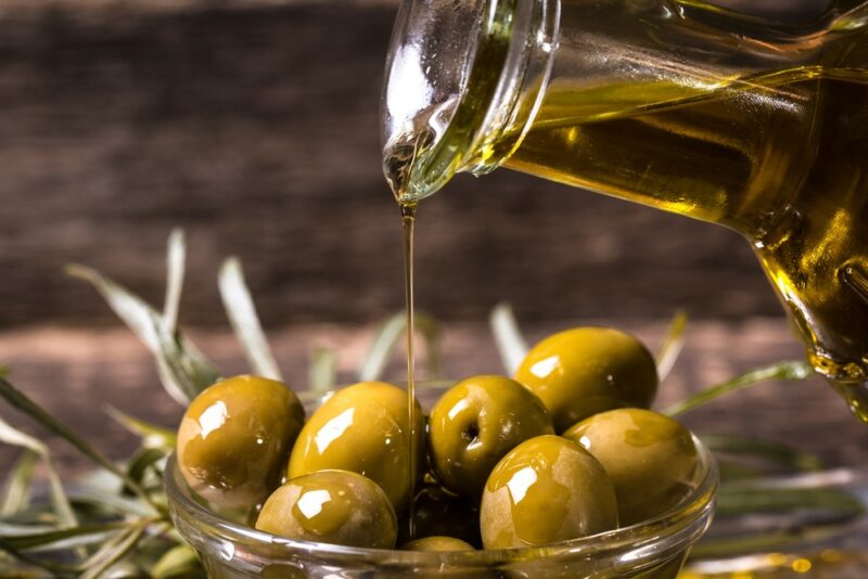 A bowl of olives that someone is pouring fresh olive oil into