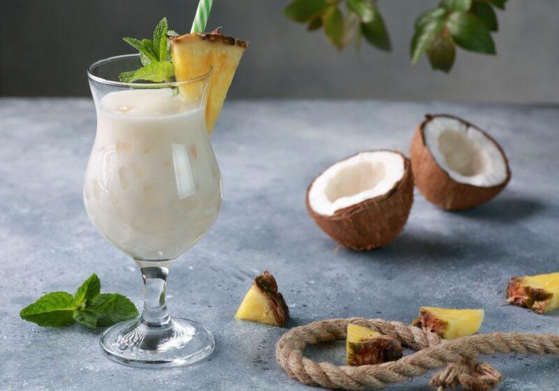 A regular pina colada in a hurricane glass, next to two coconut halves