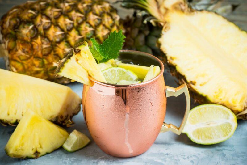 A copper mug containing a pineapple Moscow mule, surrounded by pineapples