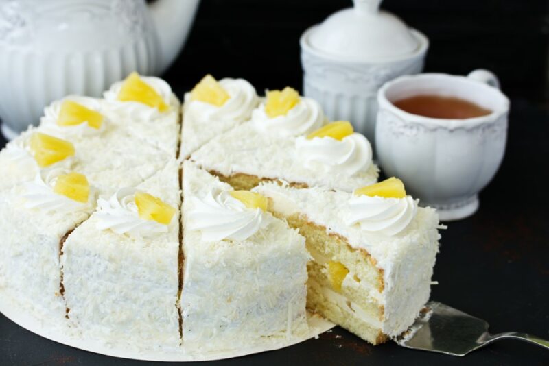 A white plate with a pineapple and coconut cake that has been cut into slices