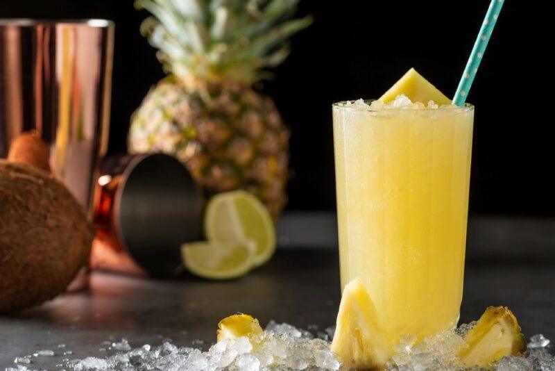 An icy pineapple cocktail called the grande finale, next to a shaker, pineapple, coconut, and lime