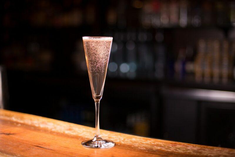 A glass contianing a pink lychee bellini on a bar