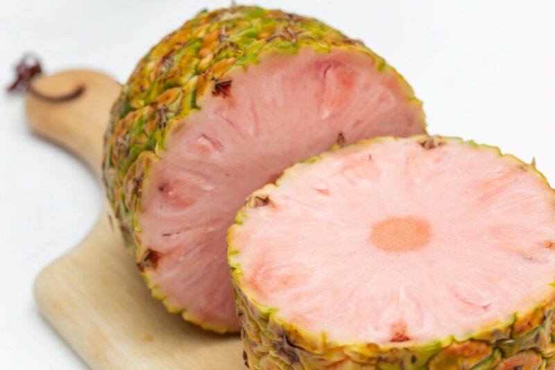 A wooden board showing a single pinkglow pineapple that's been cut in halfagainst a white background