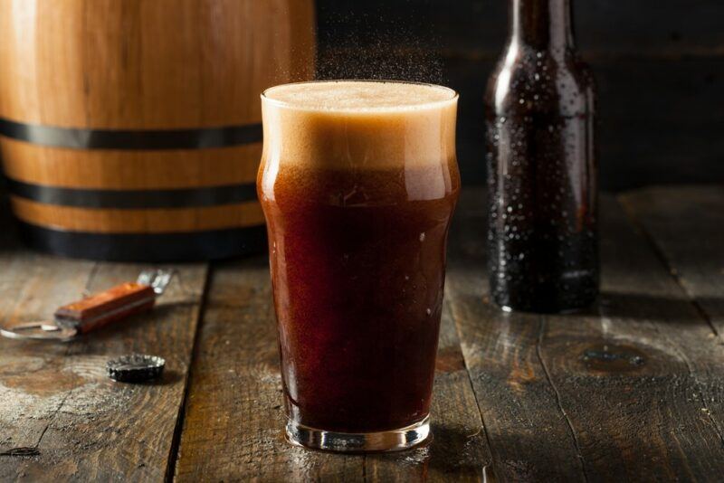 A pint glass containing a Fireball root beer cocktail next to a bottle and a barrel