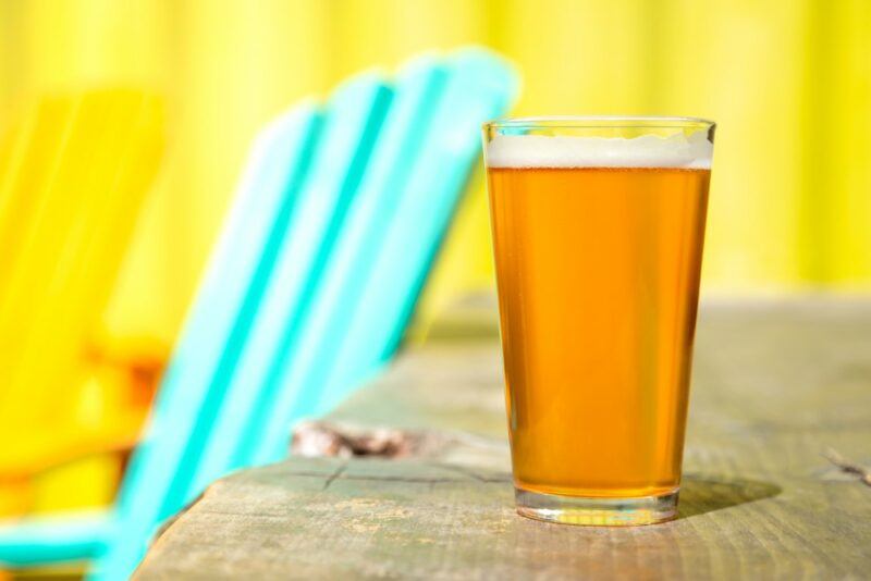 A wooden bench with a pint glass of wheat beer next to a chair