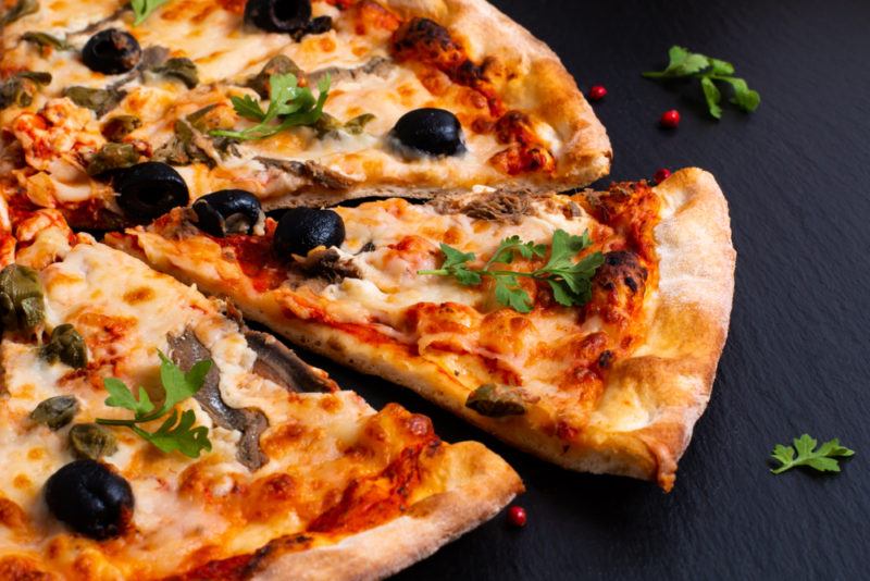 A black tabletop with a pizza that has anchovies and olives