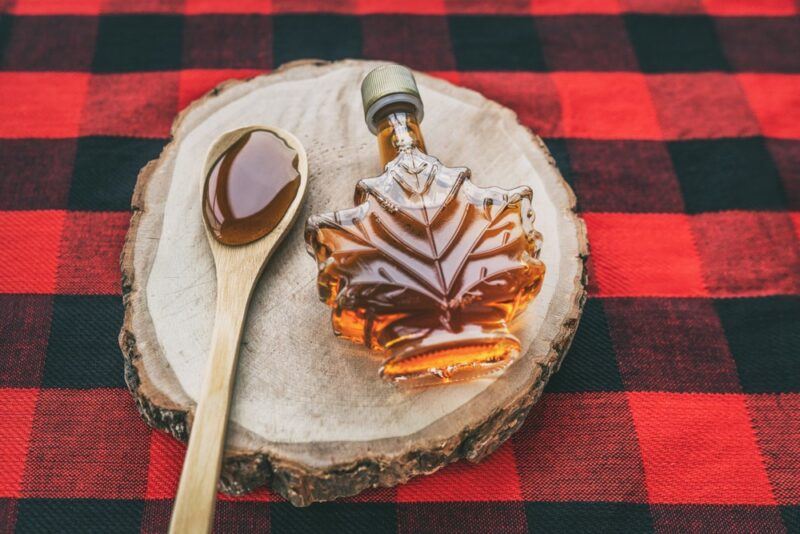 A tartan cloth with a log that has a bottle of maple syrup and a spoon