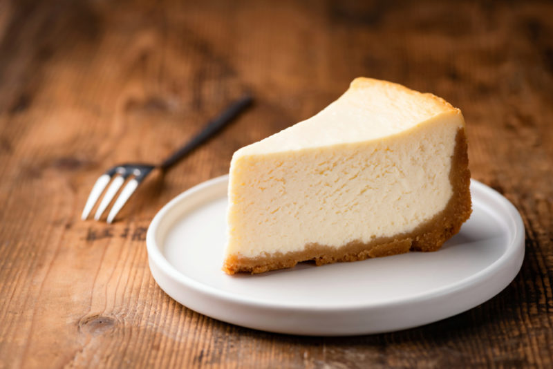 A plain cheesecake on a white plate next to a fork