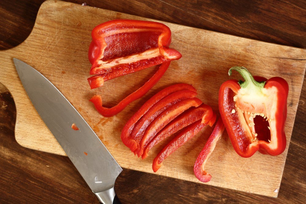 A wooden board with a bell pepper that's been cut in half and into slices