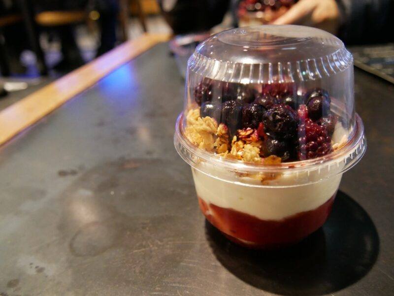 A plastic container containing a yogurt parfait with plenty of yogurt, fruit puree, and fresh berries on top