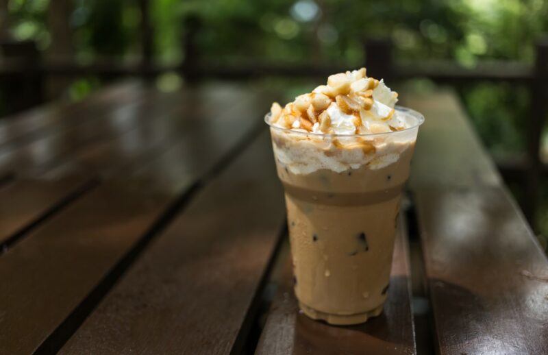 A plastic glass containing a chocolate shake with cream and macadamia nuts