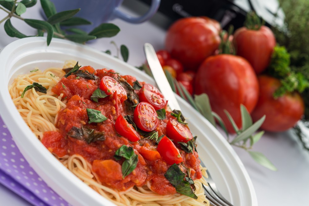 A white plate with noodles, marinara sauce, and tomatoes