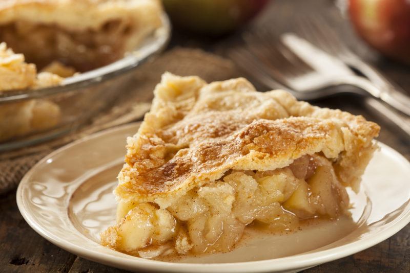 A plate of apple pie with the rest of the pie in the background