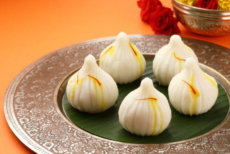 A silver plate with a green interior, containing five pieces of a dessert called modak