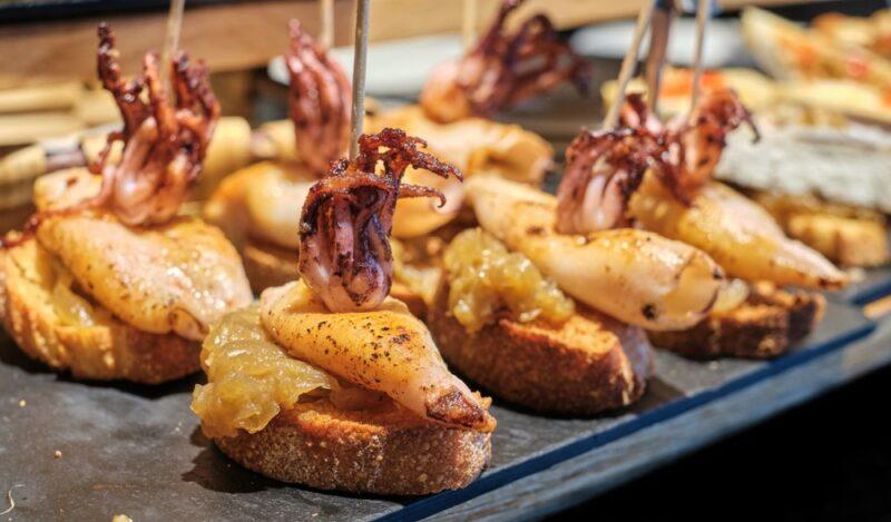 A tray with a selection of Spanish tapas known as pintxos. The tapas have bread as a base and fillings that are attached with toothpicks