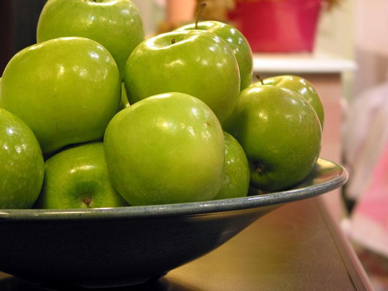 a shallow ceramic bowl full of ripe green apples