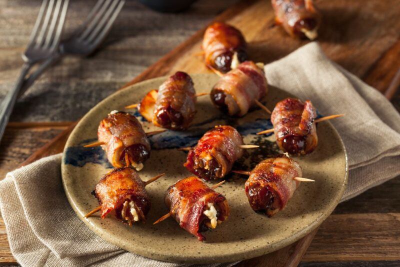 A brown plate with dates wrapped in bacon on a cloth