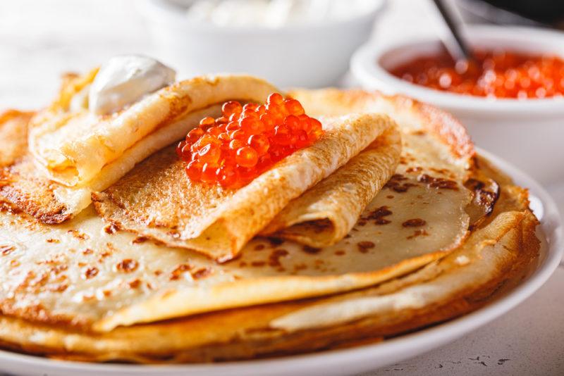 A white plate with think blinis that are topped with caviar and sour cream