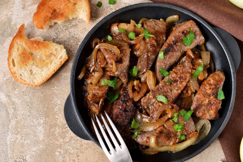 A black bowl or pan with cooked liver and a fork