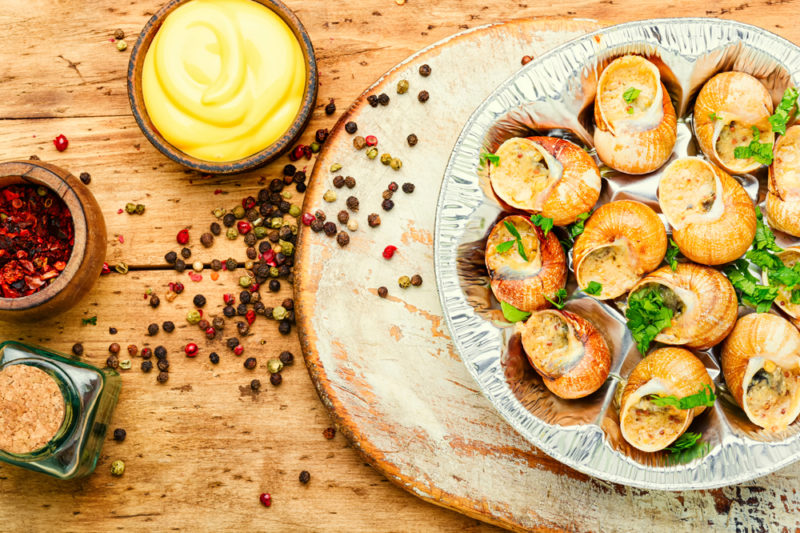 A white plate of escargot cooked in butter, next to sauces