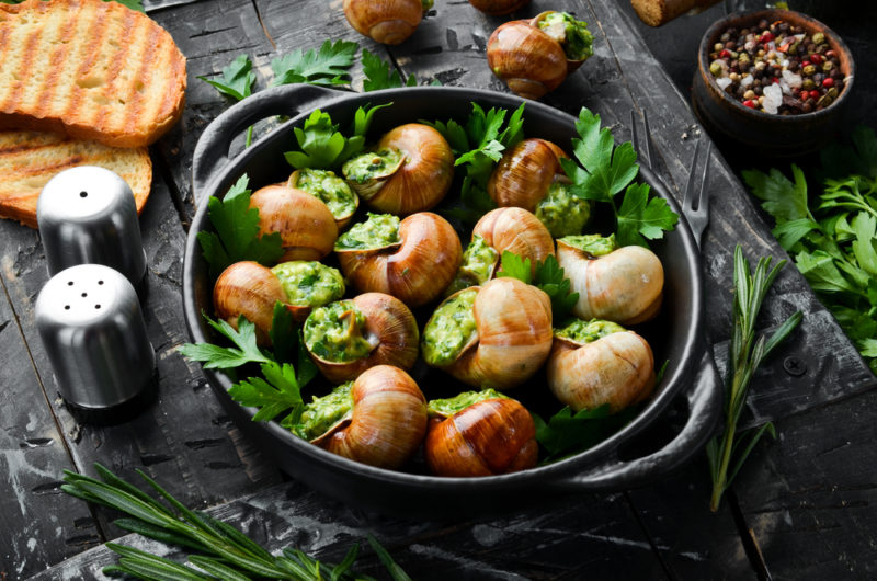 A black pan with various escargot that have been cooked in garlic butter