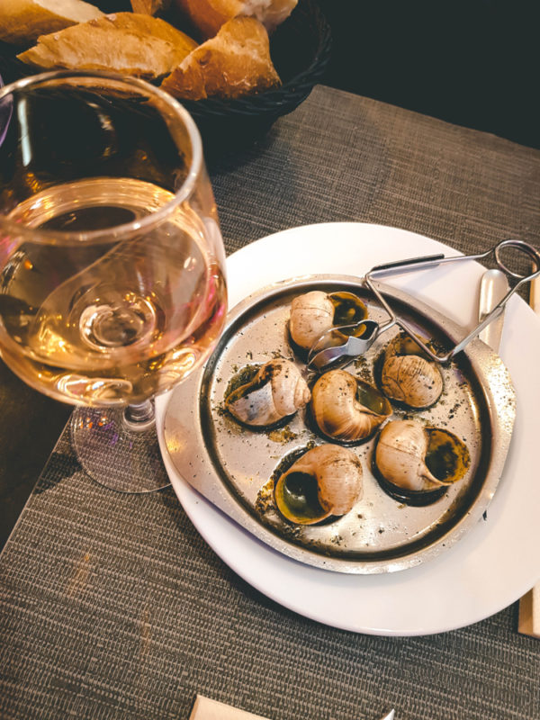 A white plate of escargot next to a glass of chardonnay on a table