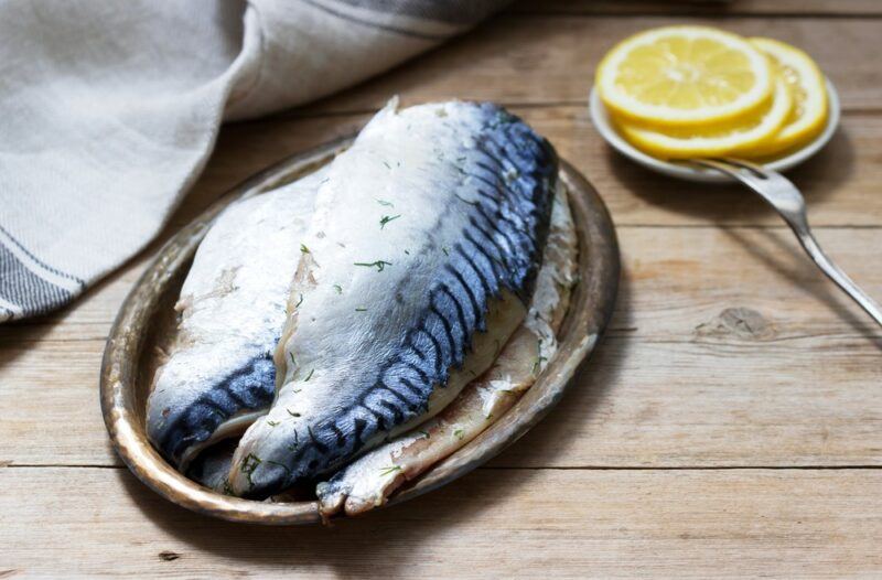 A plate of mackerel on a wooden table, next to some sliced lemons