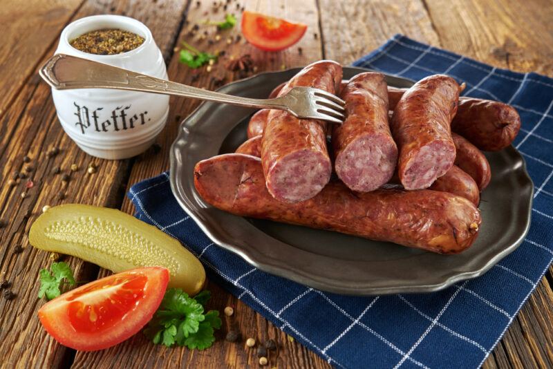 A dark plate with Polish sausages, next to a condiment and some fresh tomatoes