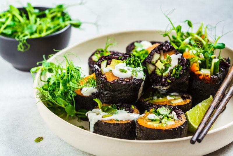 A plate of vegan sushi with seaweed, next to a small bowl of seaweed