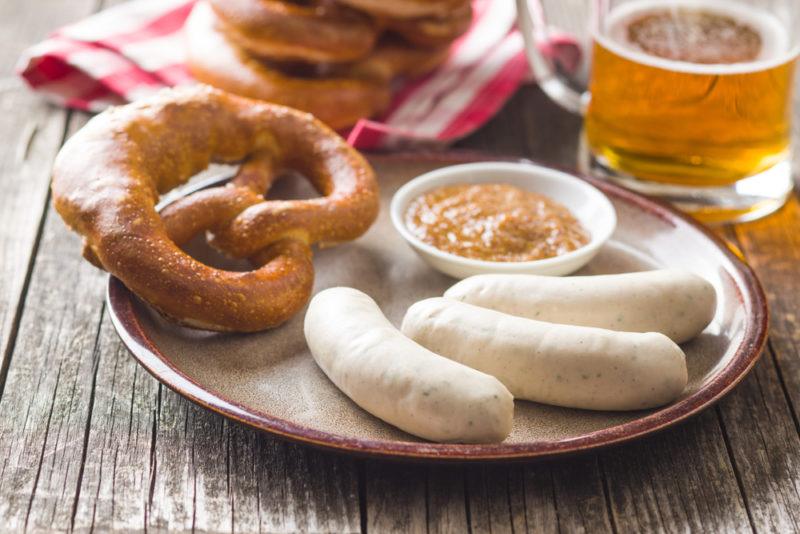 A plate with German sausages, a pretzel, and mustard, and a mug of beer in the background.