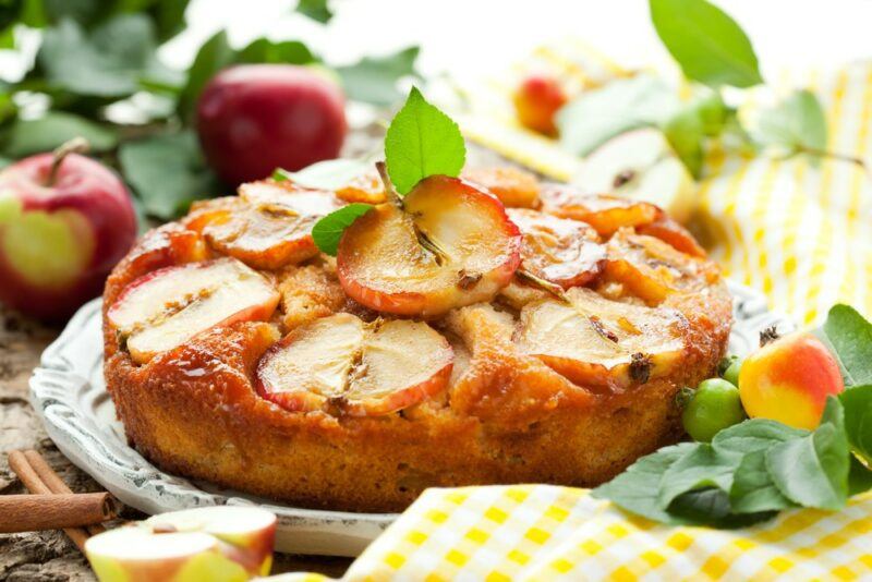 A fresh caramel and apple cake on a tray, with fresh apples in the background