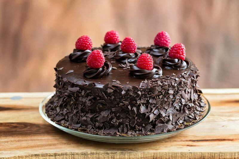 A plate with a raspberry and chocolate cake, with fresh raspberries on the top