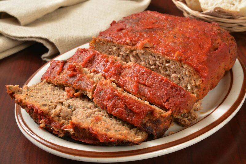 A brown and white plate with meatloaf that has been sliced into pieces