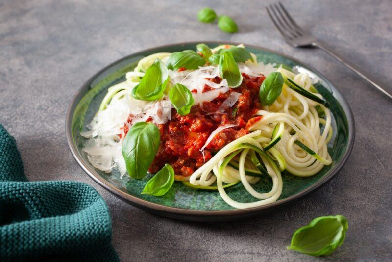 A teal plate with zoodles, meat sauce, and basil leaves