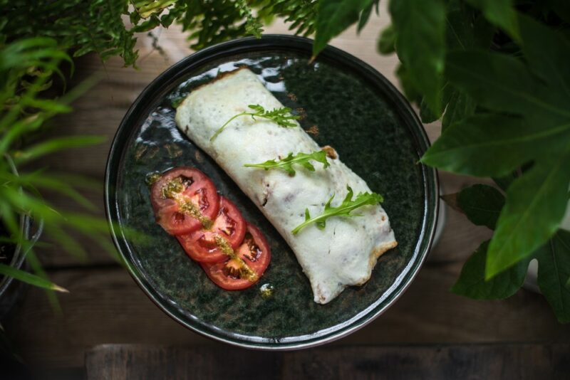 A black plate with an egg white omelet and three tomato slices, surrounded by greenery