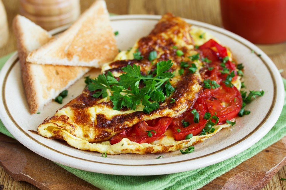 A white plate with a veggie omelet, next to some toast