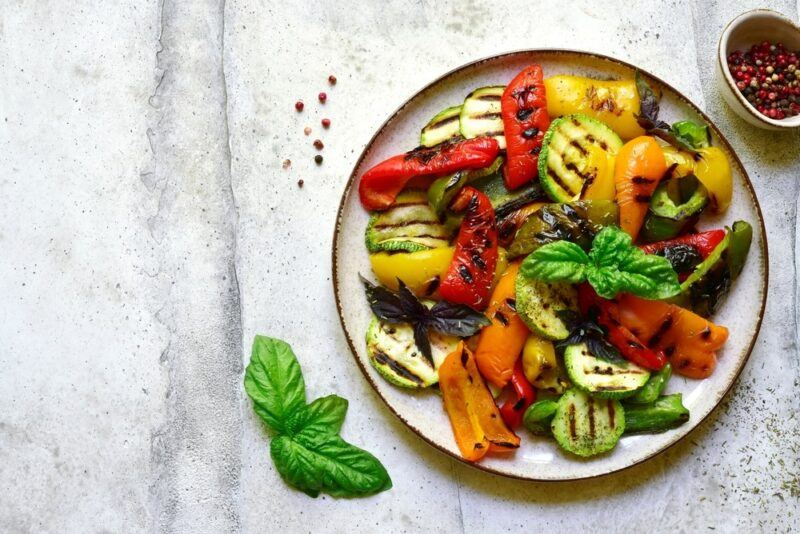 A white dish filled with grilled peppers, zucchini, and other types of summer vegetables