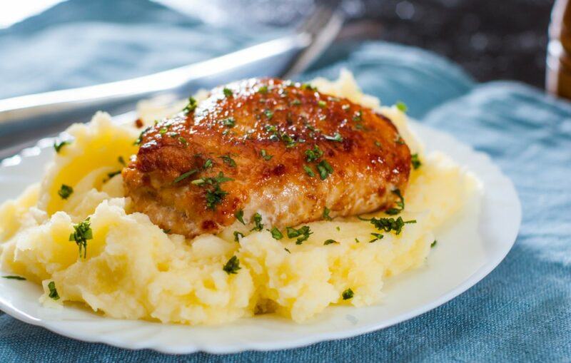 A white plate with a bed of mashed potatoes and a piece of cooked chicken