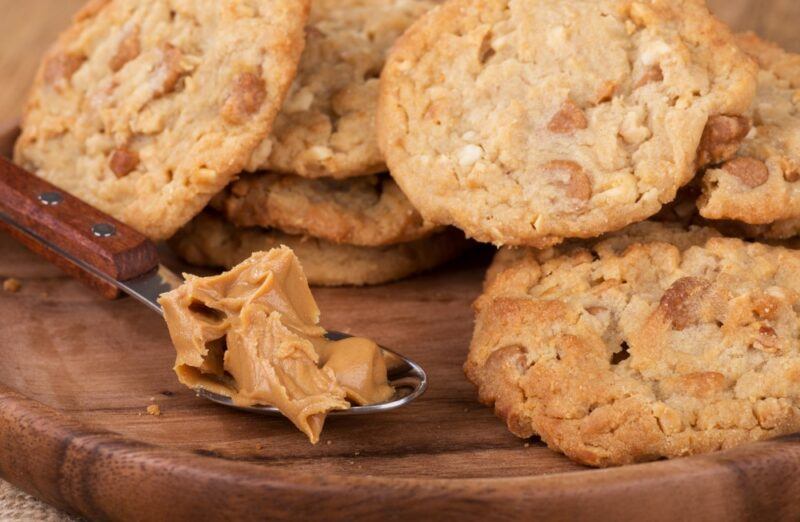 A wooden board with miso peanut butter cookies, with a spoonful of peanut butter as well